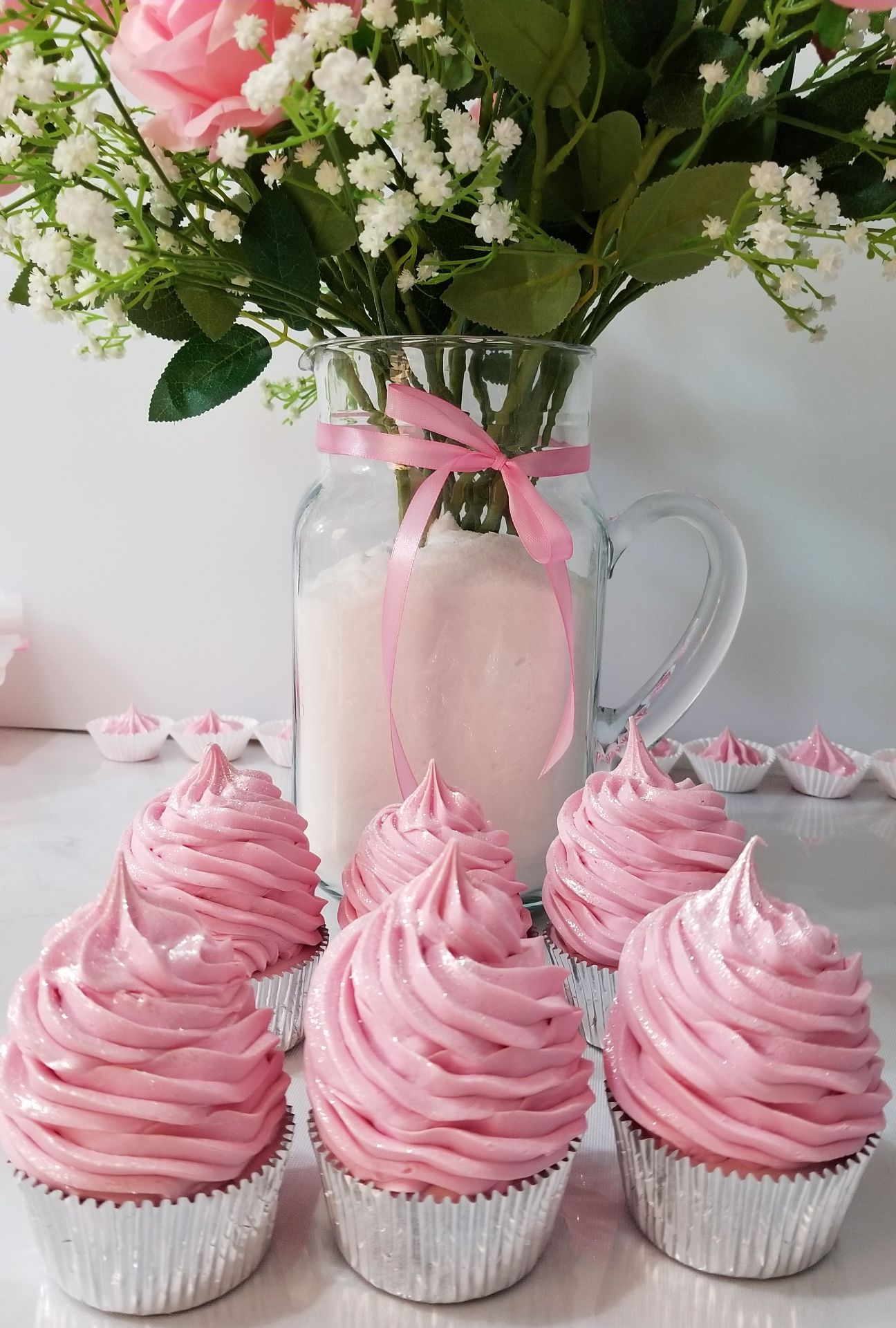 Pink cupcakes on a white table in front of pink flowers.